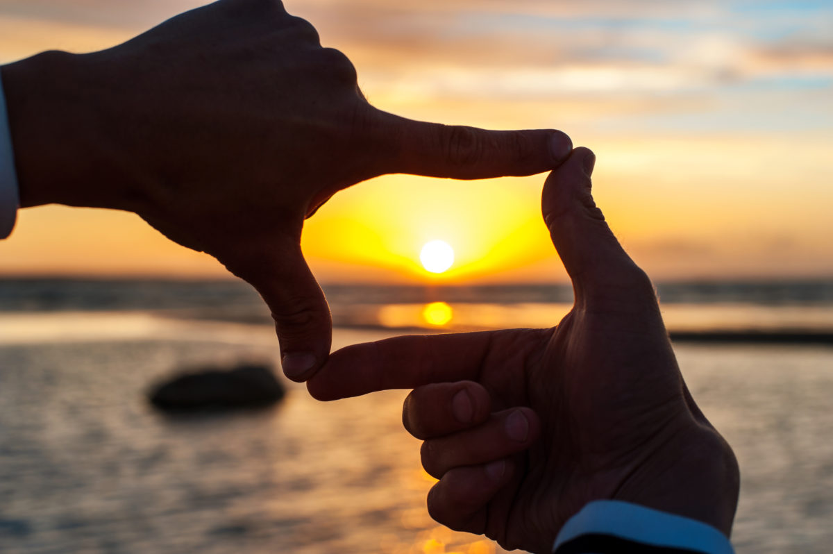 Hands forming a finger frame around a sunset over water.